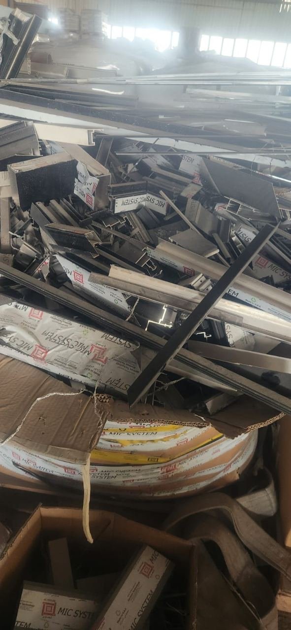 Mixed aluminium profile scrap and packaging piled in a fabrication workshop